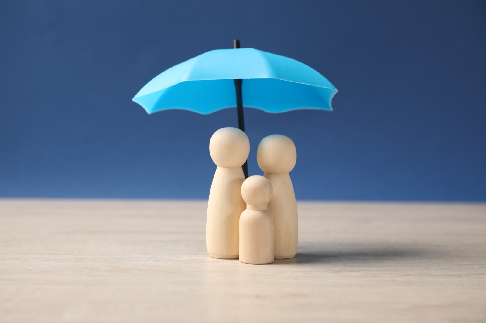 Wooden family figures under a protective umbrella